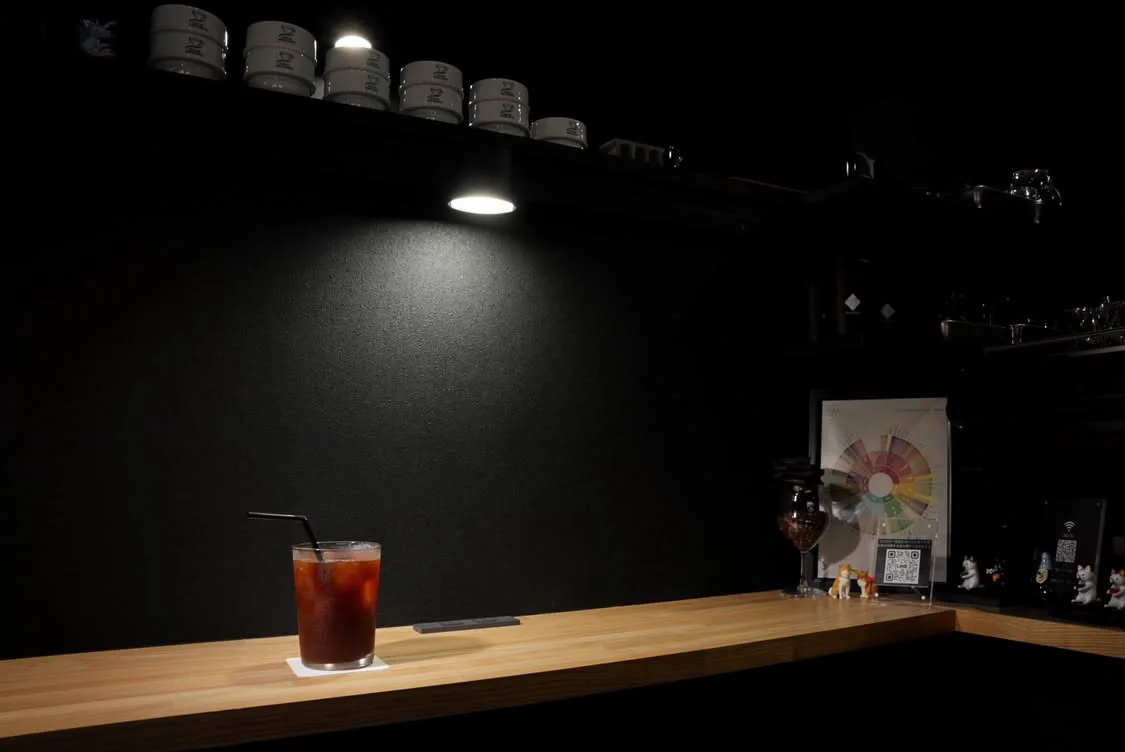 黒い店内の木のカウンターに置かれた一杯のアイスコーヒー